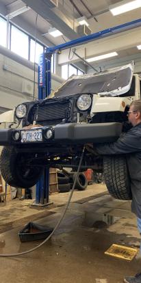 Person works on car that is raised up, reaching around a tire