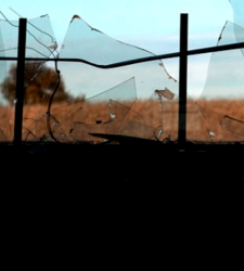Cracked glass window. Outside the window is a field of golden grass with a tree in the distance
